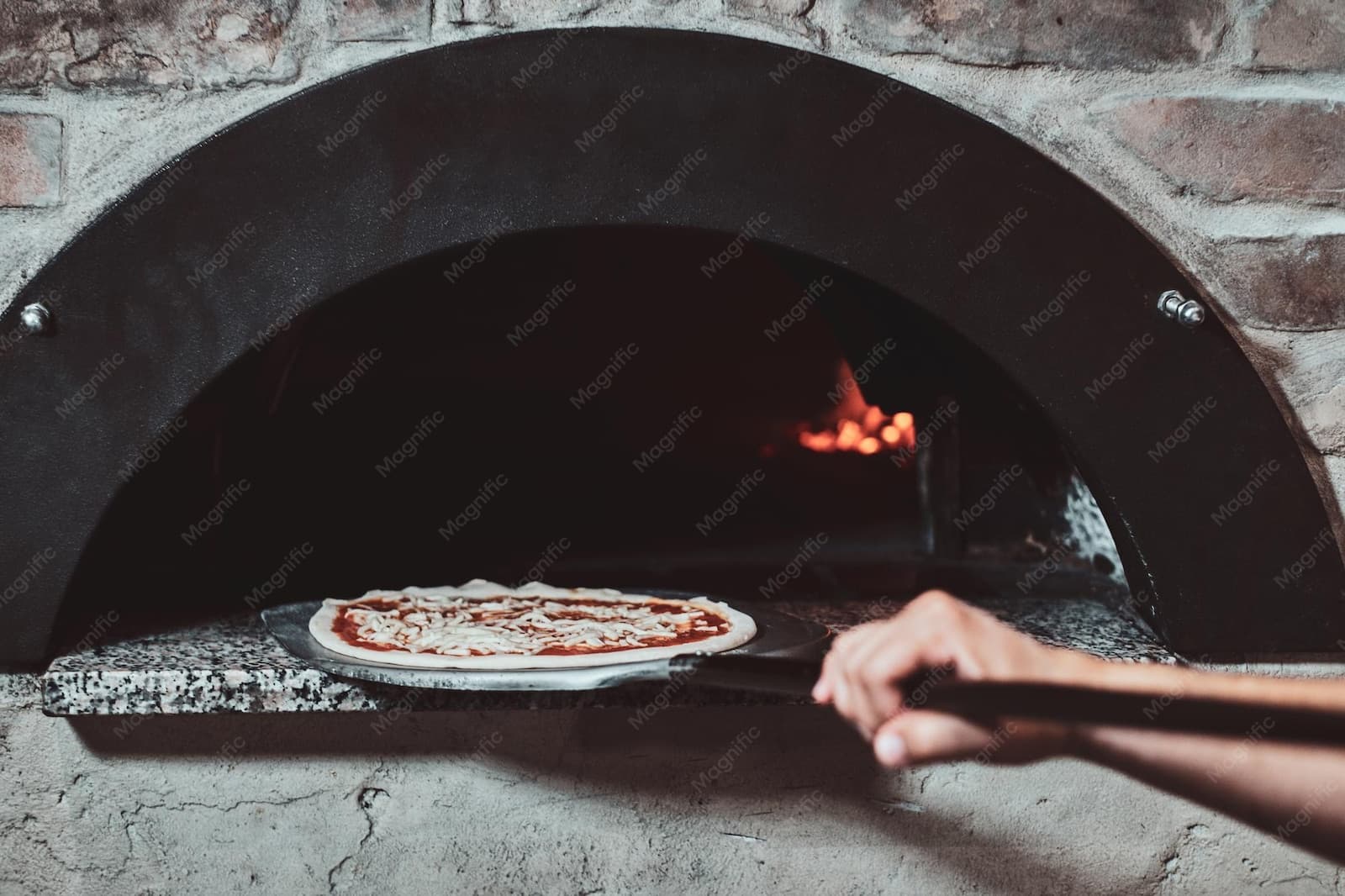 Pizzero metiendo una pizza al horno a leña con llama